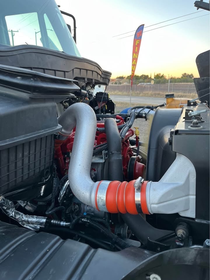Close-up of a red engine with chrome turbo piping and white ducting displayed at an outdoor automotive event