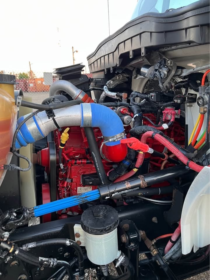 Exposed engine bay of a truck showing a red diesel engine with blue intake manifold and various mechanical components