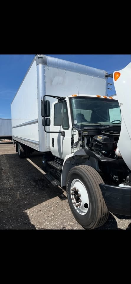 White box truck with black cab and dual rear wheels parked on gravel lot under clear blue sky