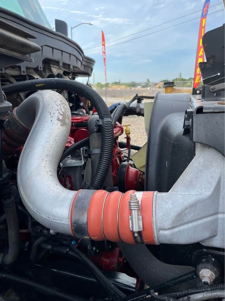 Close-up of heavy equipment engine showing curved intake pipe with red bands and red internal components at construction site