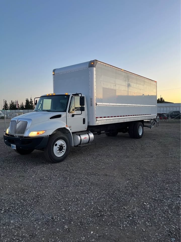 White International box truck parked on gravel lot at dusk