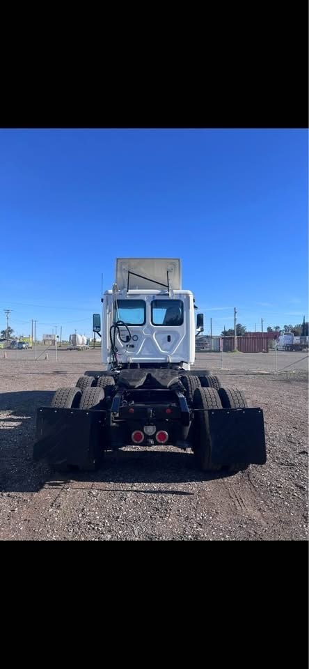 White semi truck viewed from rear on industrial lot with clear blue sky and distant buildings