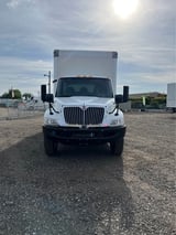 White International box truck parked on gravel lot during daytime with cloudy sky in background