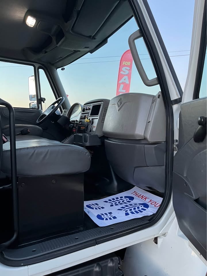 Interior of a truck cabin with open passenger door, steering wheel, dashboard, and a For Sale sign visible through the windshield