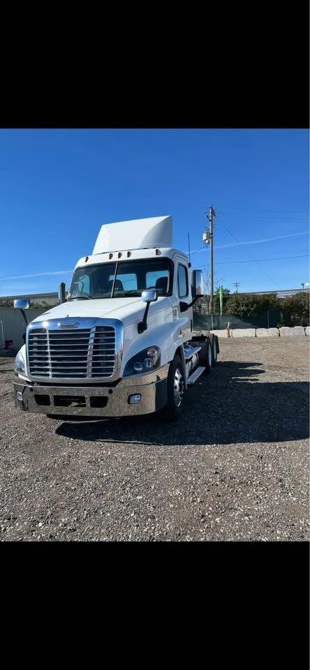 White Freightliner semi-truck with sleeper cab parked on gravel lot under clear blue sky