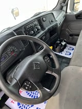 Interior view of a truck cabin showing steering wheel, dashboard, instrument cluster, and center console with controls