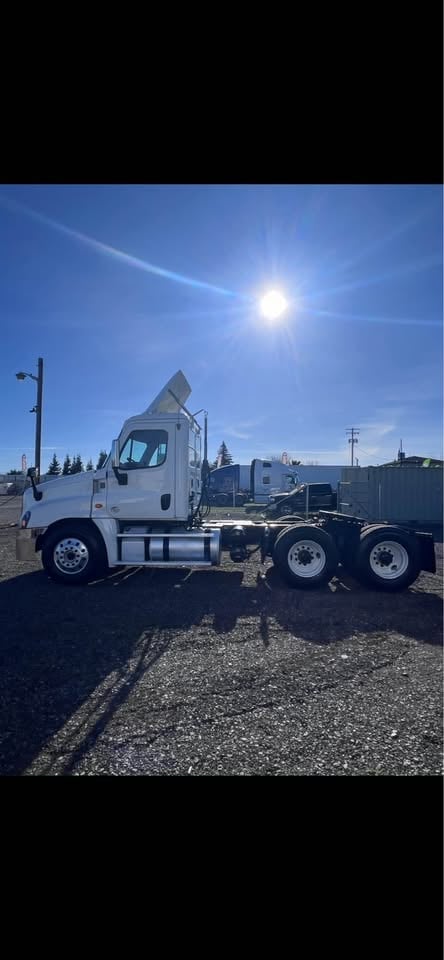 White semi truck with dual axles parked at an industrial facility under bright sunny skies