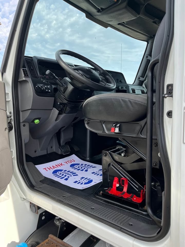 Interior view of white delivery truck cab with open driver door, steering wheel, and thank you sign on floor