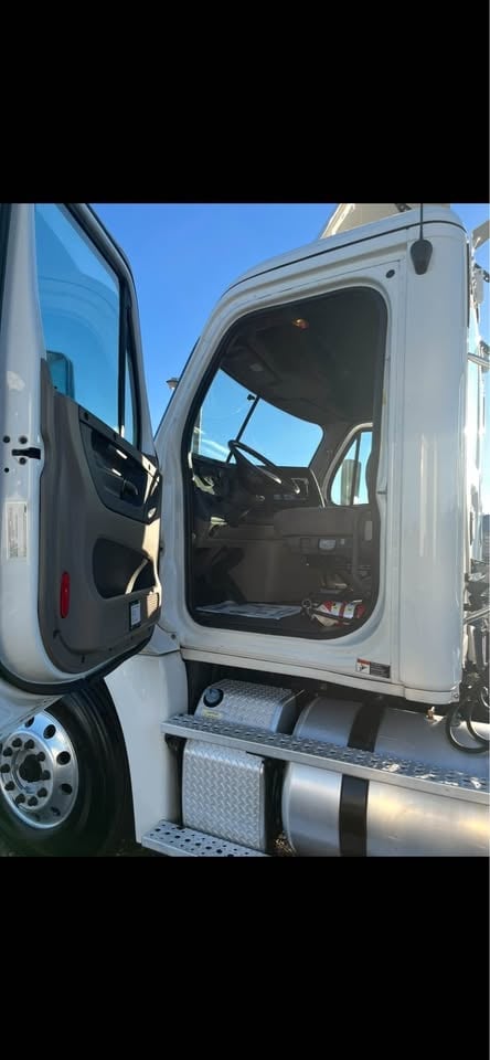 White semi-truck cab with open drivers side door showing black interior and windshield against clear blue sky