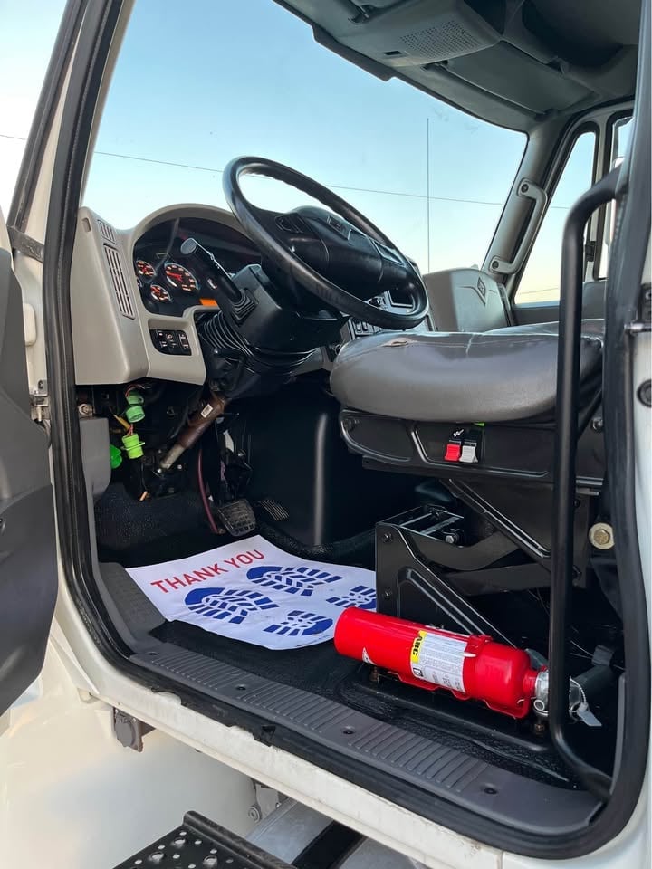 Interior view of a white truck cab showing steering wheel, dashboard, and emergency equipment including safety cones and signage on the floor