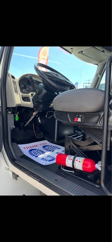 Interior view of a truck cab with steering wheel, seat, thank you sign, and red traffic cones visible through open door