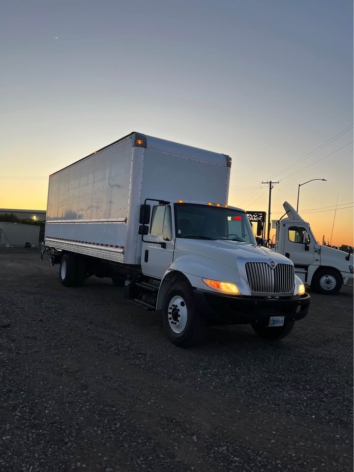 White International box truck parked in lot at sunset with other trucks visible in background
