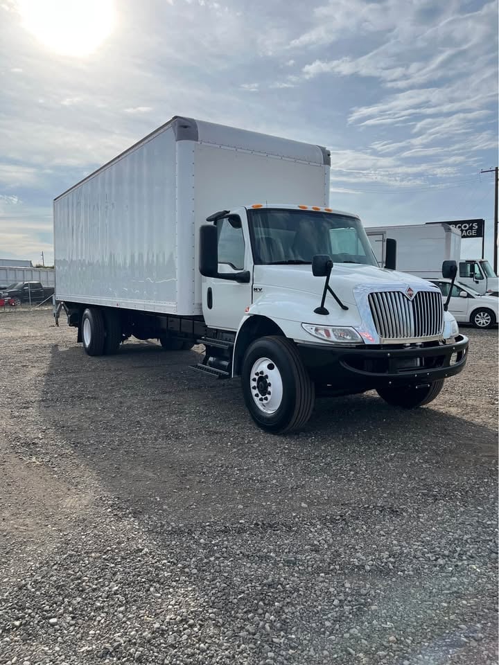 White International box truck parked at a lot on a sunny day with clouds