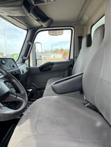 Interior of a truck cab showing steering wheel, gray seats, and windshield view of a parking lot